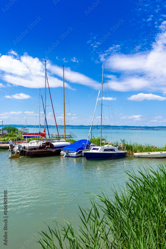 Yachts are moored to the shore of a lake with turquoise water.