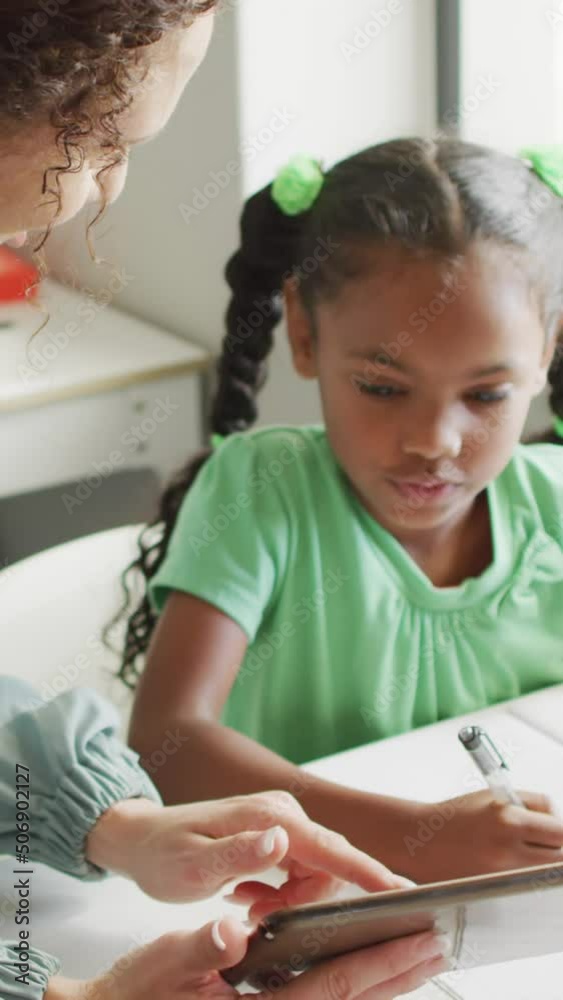 Video of happy caucasian female teacher explaining lesson on tablet to african american girl