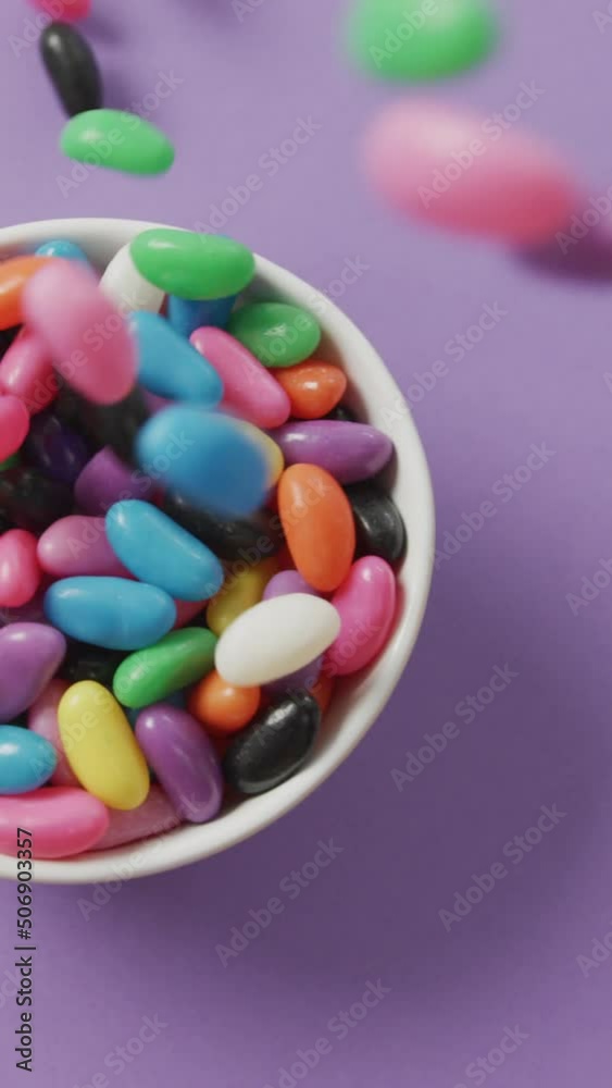 Video of close up of multi coloured sweets falling into bowl over purple background Video of close up of multi coloured sweets falling into bowl over purple background