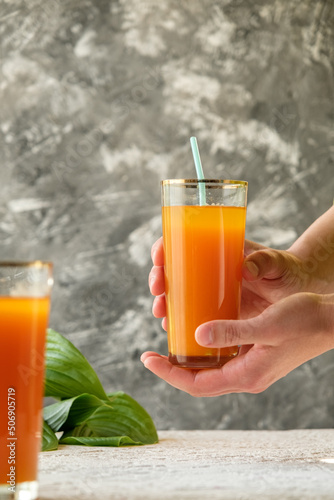 pumpkin juice with orange, hold a glass of juice in hand, human hand, two glasses with juice on a concrete table, rays of the sun, creative photo of a drink for a magazine, space for text
