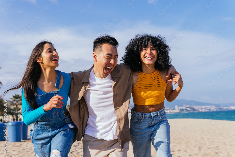 Cheerful multiracial friends hugging and walking on beach Cheerful multiracial friends hugging and walking on beach