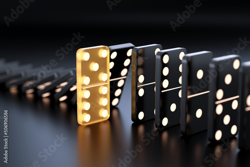 Unique yellow glowing domino tile among many black dominoes photo