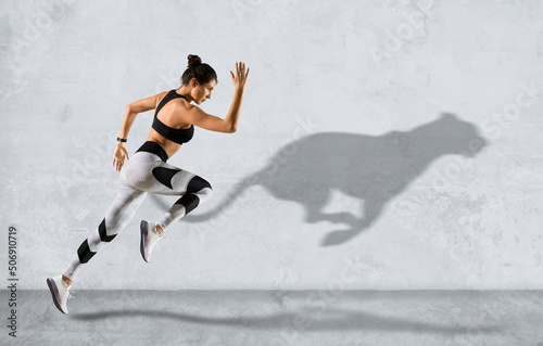 Sporty woman running on grey wall background wearing in sportswear