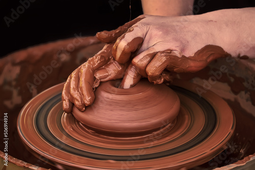 Potter's hands while working on a potter's wheel. A lump of red clay turns into a pot. The process of forming a ceramic product