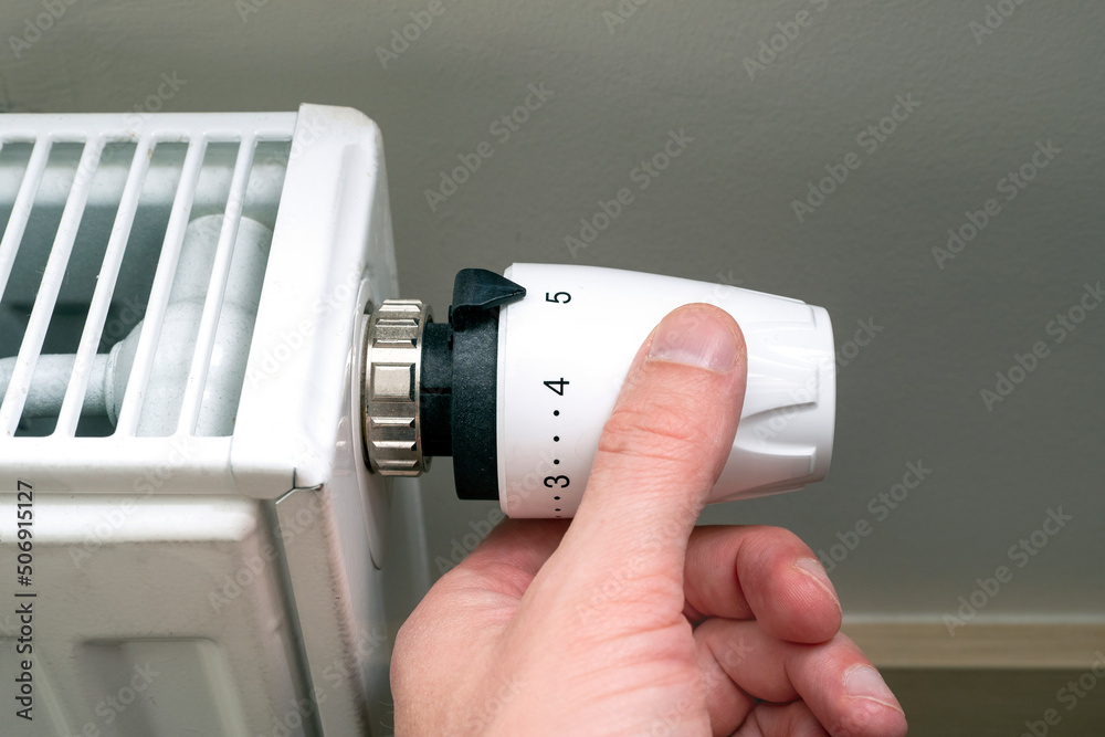 Close-up of hand and heat radiator knob, concept picture about heating season and energy saving Close-up of hand and heat radiator knob, concept picture about heating season and energy saving