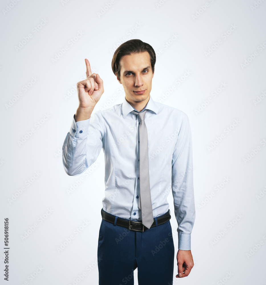 Warning concept wih young handsome man in white shirt with raising hand and forefinger isolated on light grey wall background, close up Warning concept wih young handsome man in white shirt with raising hand and forefinger isolated on light grey wall background, close up
