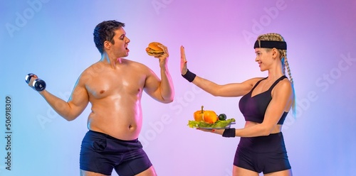 Fat man chooses between burger and fitness with dumbbells. Trainer girl tells him stop and gives vegetables instead of fast food. Not sporty men eating hamburger isolated on pink background.