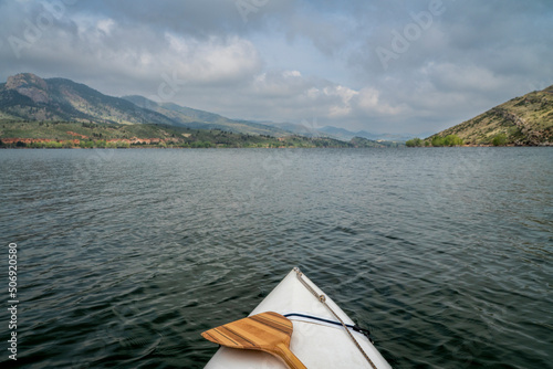 bow of a decked expedition canoe with wooden paddle on a mountain lake, paddler view - Horsetooth Reservoir in northern Colorado