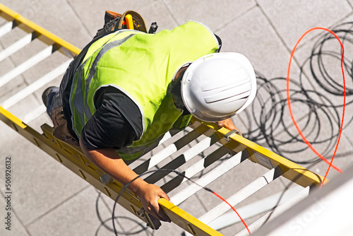 electrician worker on staircase installing optical fiber cable for internet and telephone lines in city street