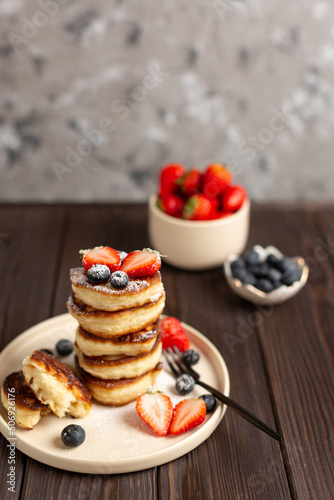 Fresh pancakes laid out in a stack, decorated with fresh berries, sprinkled with powdered sugar, beautiful serving