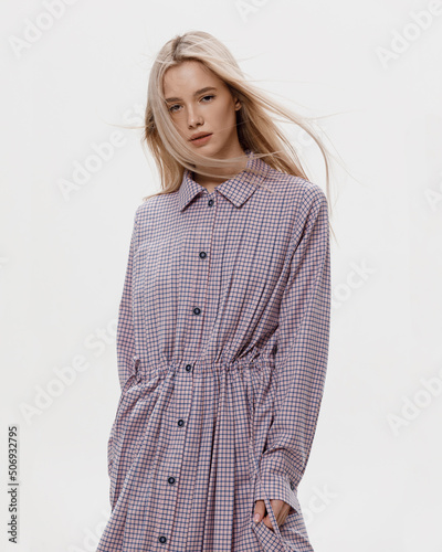 Studio photoshoot of a smiling young blond woman wearing casual clothing against a white background.  Natural makeup and hairstyle