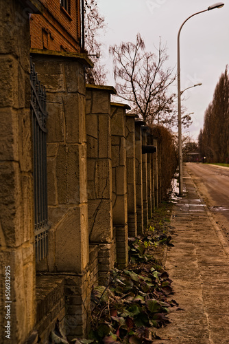 Ogrodzenie z cegły , kamienia ( piaskowiec ) oraz stalowych prętów , biegnące wzdłuż ulicy z latarniami wczesną wiosną .