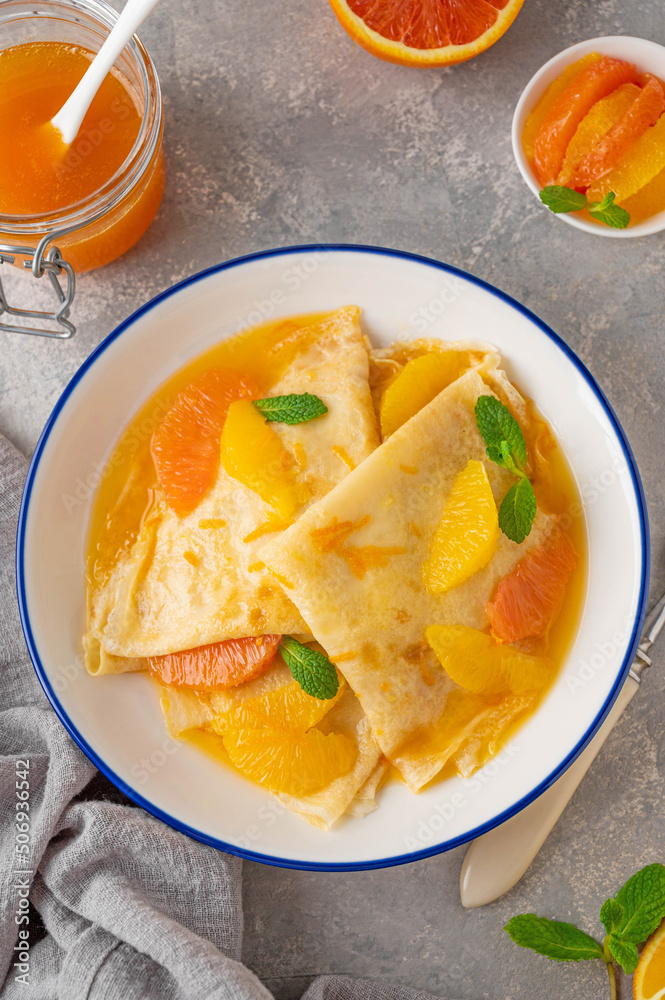 Delicious crepes suzette with orange syrup and slices fruits on a plate on a gray concrete background, top view Delicious crepes suzette with orange syrup and slices fruits on a plate on a gray concrete background, top view