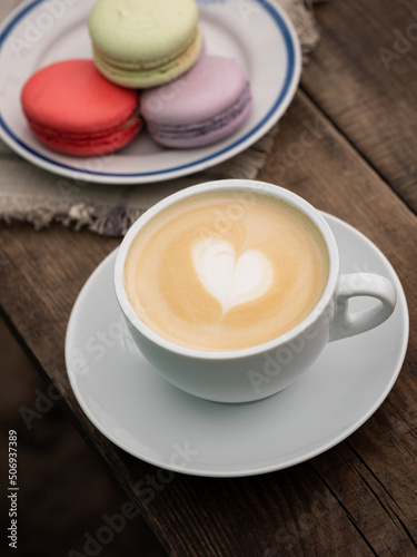 Cup of cappuccino with heart and colorful macaroons on a wooden table