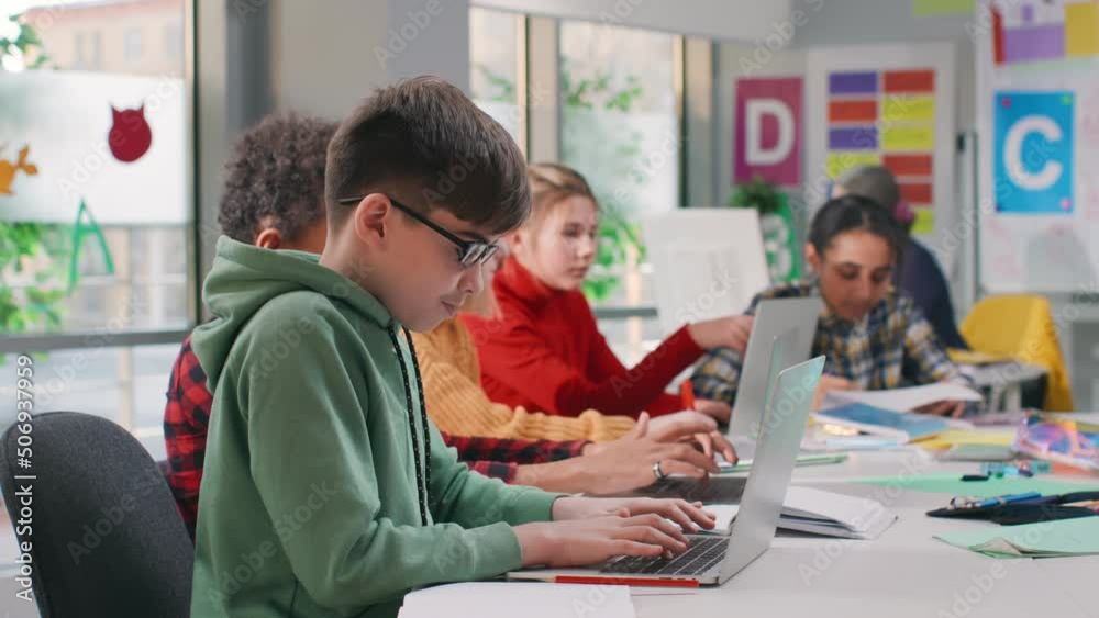 Teenage male student sit down at desk and write task in notebook using laptop