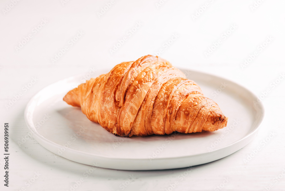 Plate with one fresh croissant on white wooden table. Plate with one fresh croissant on white wooden table.