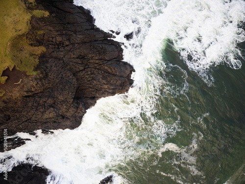 An aerial view of ocean waves crashing against a hilly shore. A beautiful piece of wild nature. Minimalism. Abstraction. Travel, tourism, postcard, banner.