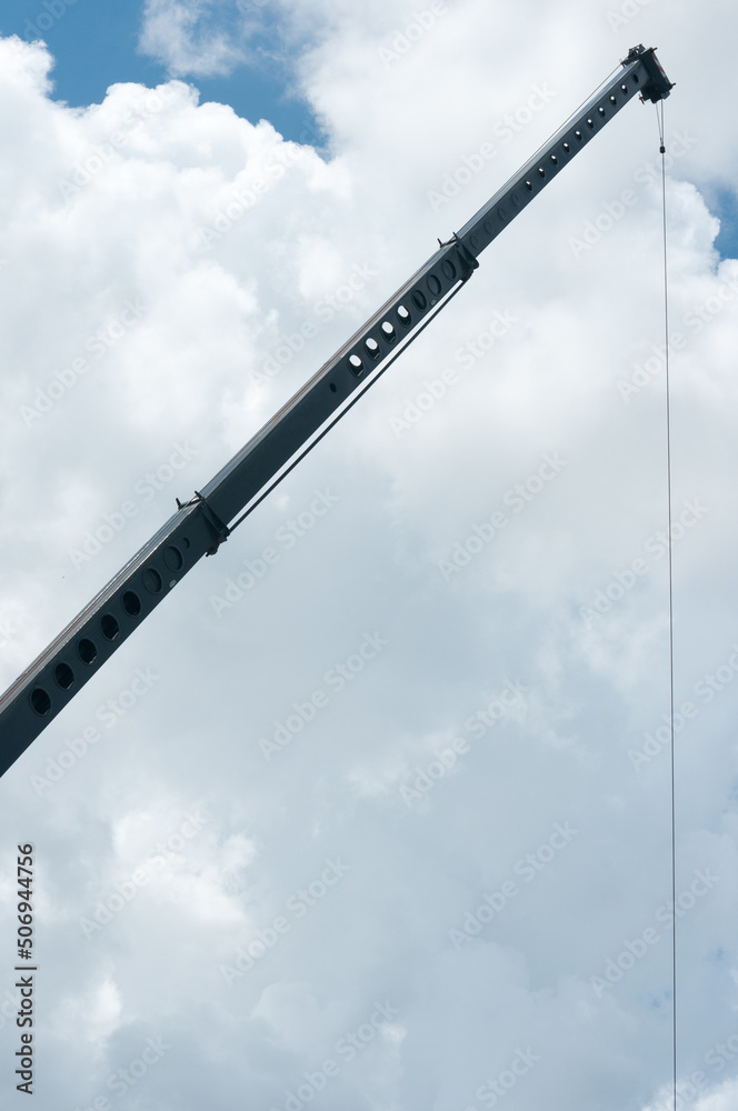 front view, far distance of a steel boom of a construction crane with a cable supporting construction equipment at a tropical, cloudy site front view, far distance of a steel boom of a construction crane with a cable supporting construction equipment at a tropical, cloudy site