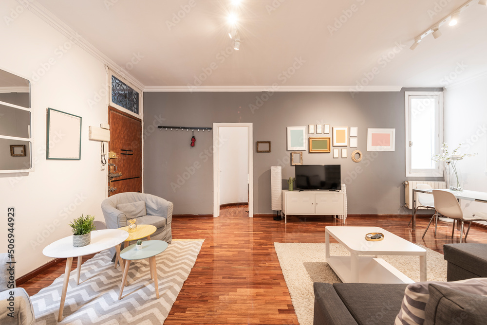 Fototapeta premium spacious living room with wingback sofas, auxiliary coffee tables, sofa bed with chaise longue, chromed metal dining table and white glass top with reddish glossy parquet flooring and gray wall