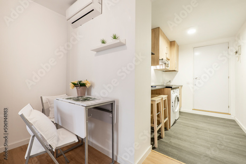 Folding white wooden dining table with matching chairs next to a kitchen in a short-term rental apartment