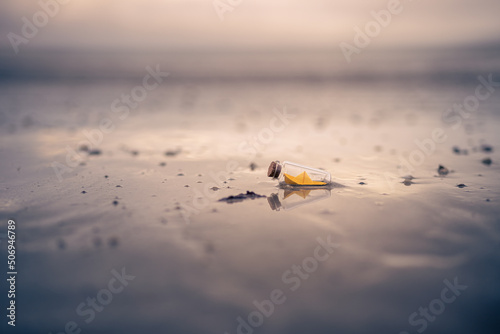 Miniature origami ship in bottle standing on sand at sunrise photo