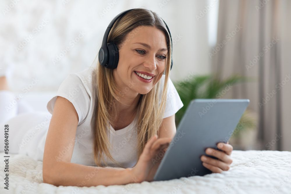Happy young woman laying in bed with tablet and headset Happy young woman laying in bed with tablet and headset