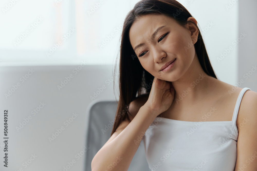 Neck pain. Suffering from fibromyalgia tanned beautiful young Asian woman rubbing massaging tensed muscles at home interior living room. Injuries Poor health Illness concept. Cool offer Banner Neck pain. Suffering from fibromyalgia tanned beautiful young Asian woman rubbing massaging tensed muscles at home interior living room. Injuries Poor health Illness concept. Cool offer Banner