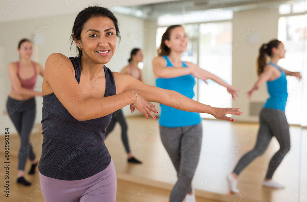 Portrait of cheerful latin american woman exercising dance moves in fitness studio