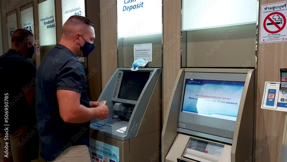A European man withdraws cash from a Thai ATM, a masked man makes transactions at a Thai bank ATM A European man withdraws cash from a Thai ATM, a masked man makes transactions at a Thai bank ATM
