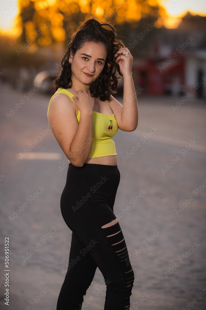 A beautiful curly haired latin poses in leggings at sunset