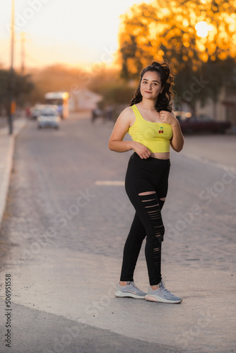 A beautiful curly haired latin poses in leggings at sunset
