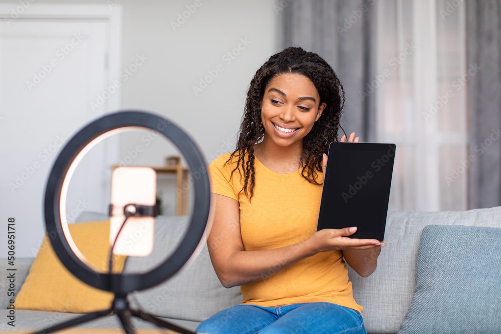 Joyful black female blogger filming video review of modern digital tablet, talking to cellphone webcamera - obrazy, fototapety, plakaty 