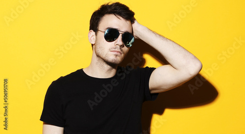 Lifestyle, fashion and people concept: Portrait of a young handsome man wearing sunglasses on yellow background © Raisa Kanareva