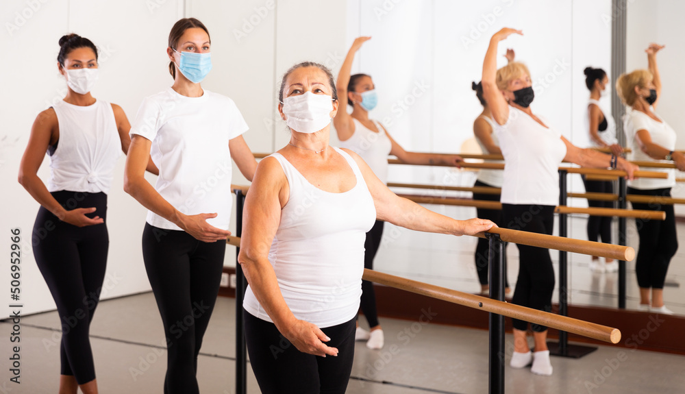 Fototapeta premium Women of different ages in face masks exercising ballet moves in training room.