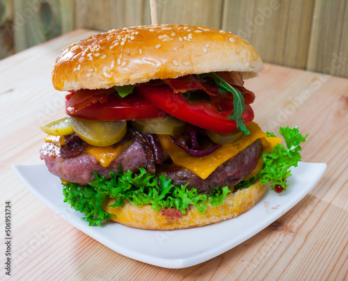 Big juicy double hamburger with cheese, fresh tomatoes, lettuce leaves, fried onion and bacon