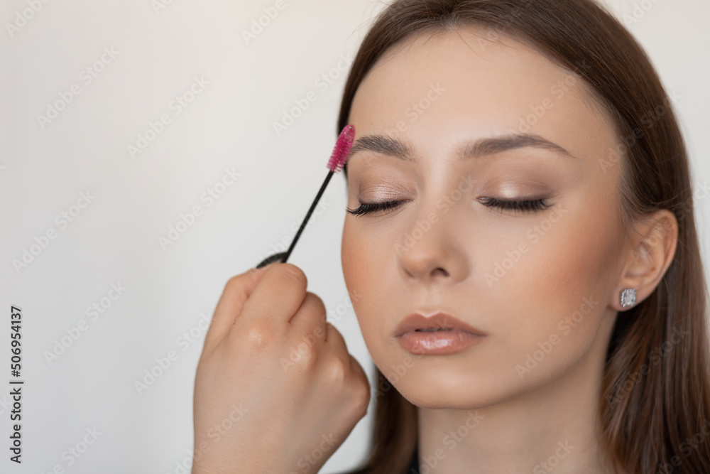 Woman face in spa salon correcting and brushing eyebrows by brush, checking brow eye line. Shine skin face. Close up