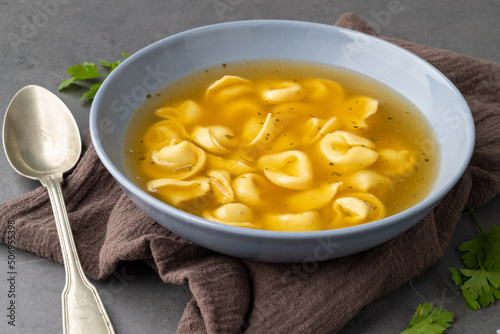 Cappelletti or tortellini brodo soup in a bowl with seasoning over stone background photo