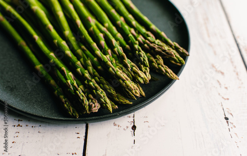 Close up of spears of fresh asparagus on a plate on white table.