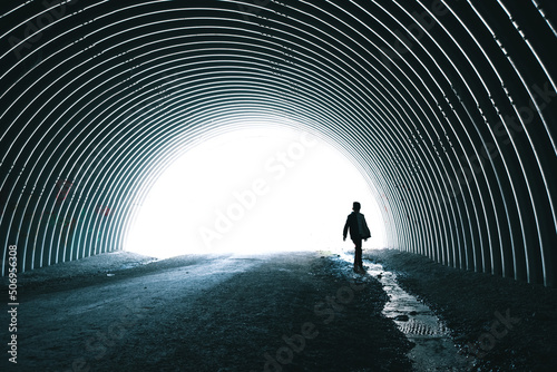 Child walking alone beside stream running through dark metal tunnel. photo