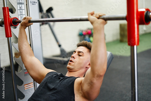 Young Man Exercising In Gym With Bench Press photo