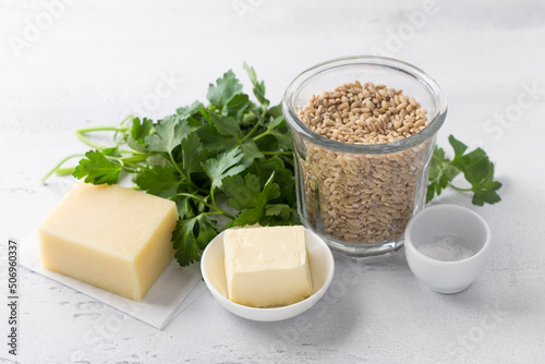Ingredients for cooking a vegetarian dish: pearl barley, cheese, parsley, butter, salt on a light gray table, top view. healthy homemade food