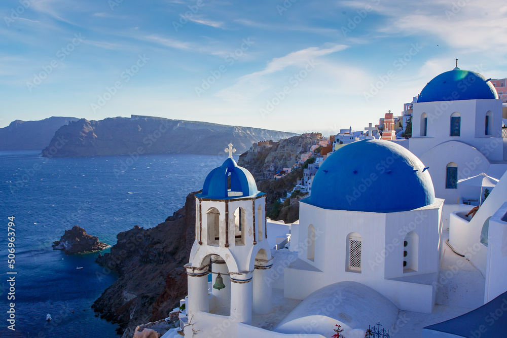 Fototapeta premium Santorini famous view. Blue domed churches on the Oia cliff with Aegean sea and Caldera in background.