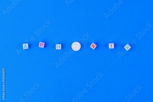 APHONIA text made in cubes, a white medical pill with a score instead of the letter O. Classic blue background photo