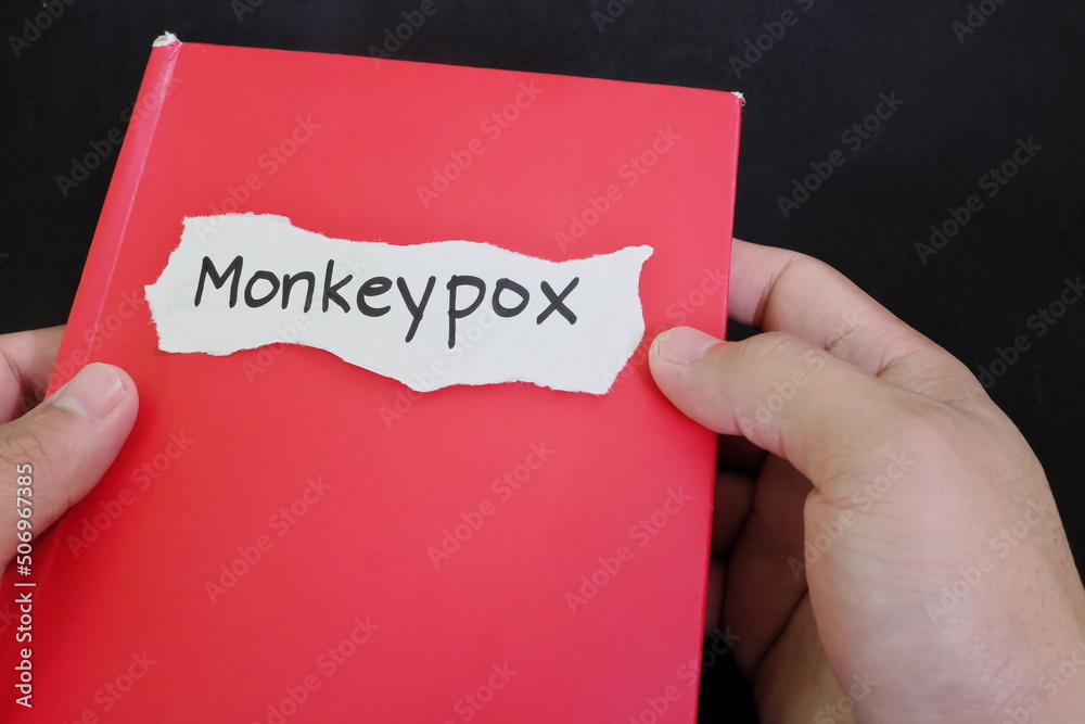 Monkeypox disease information, research and data. Human hand holding a red book about monkeypox in black background. Monkeypox disease information, research and data. Human hand holding a red book about monkeypox in black background.