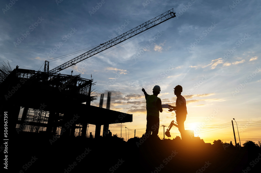 Engineers and workers inspecting projects at the construction site background. Construction site at sunset in the evening, Asian engineer silhouette