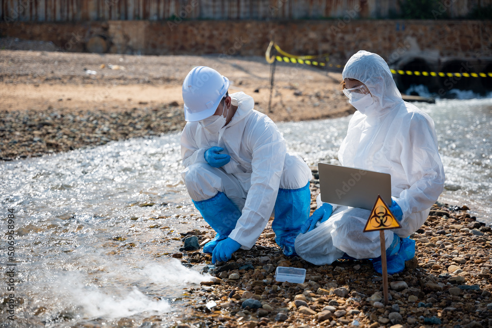 Biologist wear protective suit and mask collects sample of waste water from industry, problem environment, Ecologist sample taken dead fish to inspection and save data to laptop computer, Toxic water Biologist wear protective suit and mask collects sample of waste water from industry, problem environment, Ecologist sample taken dead fish to inspection and save data to laptop computer, Toxic water
