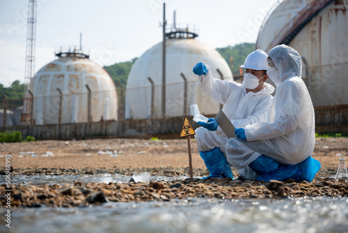 Ecologist sampling taken dead fish to inspaction and save data to laptop computer, Biologist wear protective suit and mask collects sample of waste water from industry, problem environment