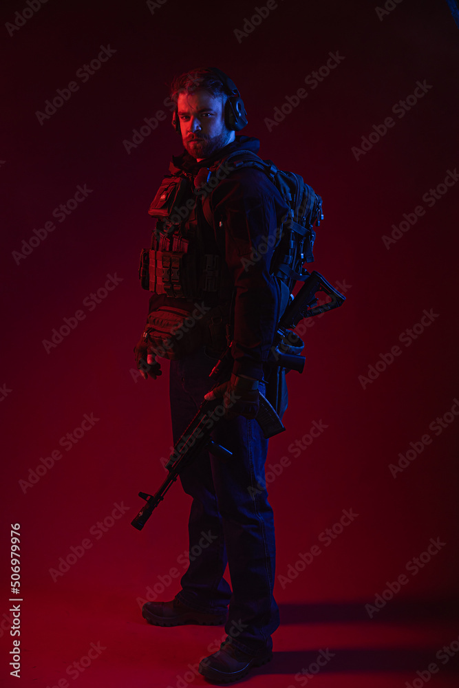 Naklejka premium airsoft player in full gear with guns GG RK74. a man in headphones, body armor, with a backpack and a belt. red background. colored, blue-red light