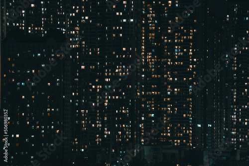 Glass facade of modern city high rise, buildings show lighting using by human activity, energy usage at night time. Glowing windows of skyscrapers at night.