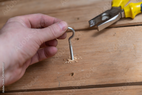 The process of screwing a half-ring screw into a board. The man's hand screws the C-shaped screws into the drilled holes. Close-up. Selective focus.
